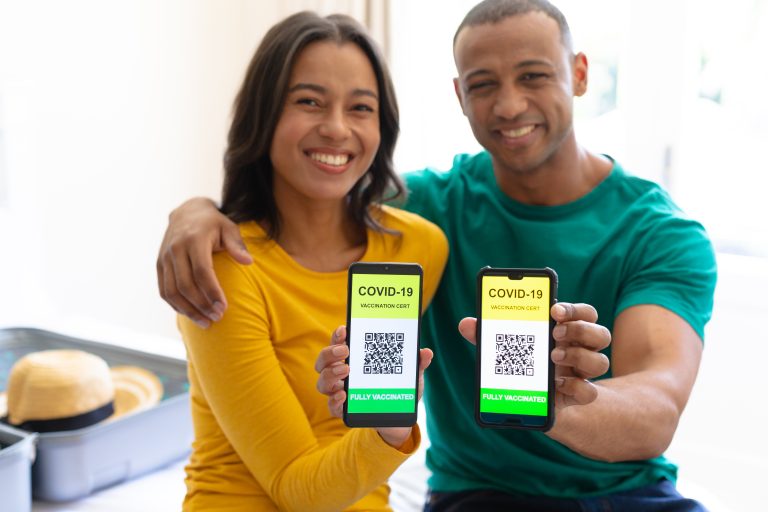 Portrait of smiling african american couple showing covid-19 vaccine certificate on smartphones. people, technology and vaccination concept, unaltered